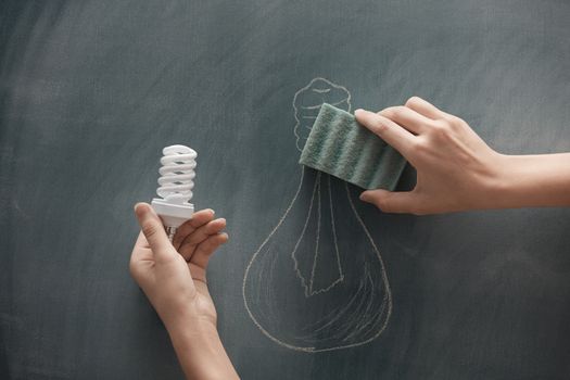 Human hand holding energy saving lamp at the blackboard with traditional lamp