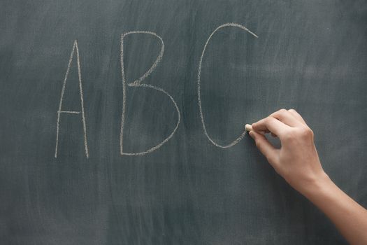 Human hand writing ABC characters on a blackboard