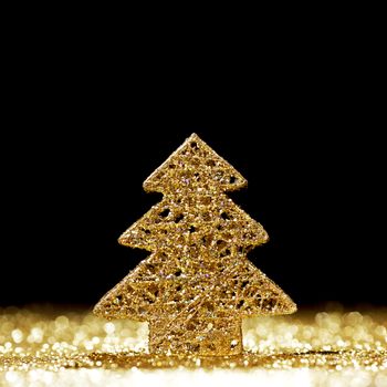 Decorative golden toy christmas tree on glitters over black background