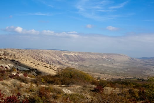 An autumn valley with bushes and blue sky
