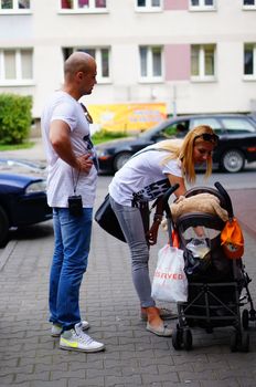 POZNAN, POLAND - SEPTEMBER 13, 2014: Man and woman standing by a baby buggy close to parked cars