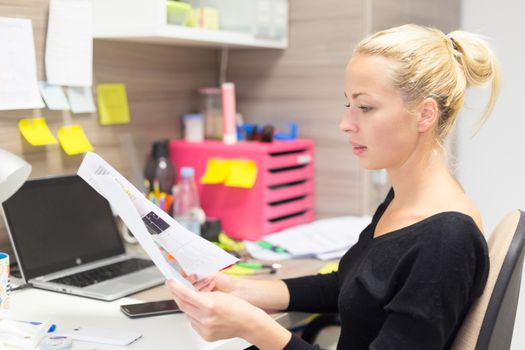 Business and entrepreneurship consept. Beautiful blonde business woman working in colorful modern creative working environment reviewing some papers. 