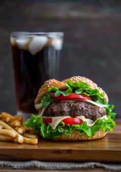 Closeup of Homemade Hamburger with Fresh Vegetables, French Fries and Drink with Ice on Wooden Background