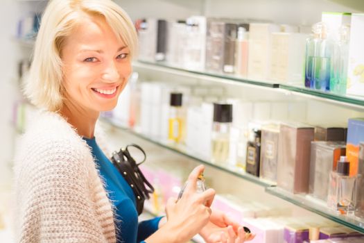 Casual blond young woman smelling perfume in retail store. Beautiful blond lady testing  and buying cosmetics in a beauty store.