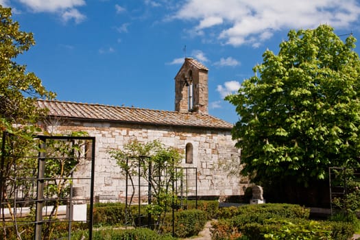 An old stone roman church and a garden in San Quirico d'Orcia in Italy
