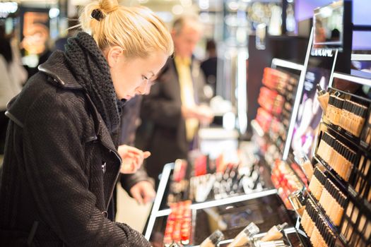 Beautiful blond lady testing  and buying cosmetics in a beauty store.