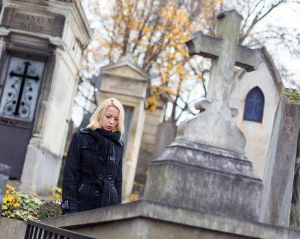 Solitary woman mourning by gravestone, remembering dead relatives in on Pere Lachaise cemetery in Paris, France.