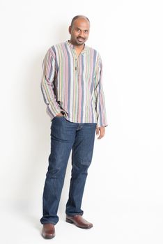 Full length confident mature Indian man in casual wear standing on plain background with shadow.