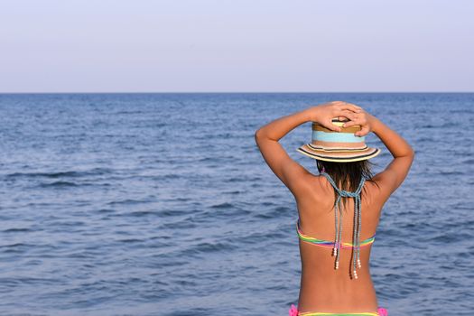 Little girl on the beach at sunset with her hands blocking a large hat.