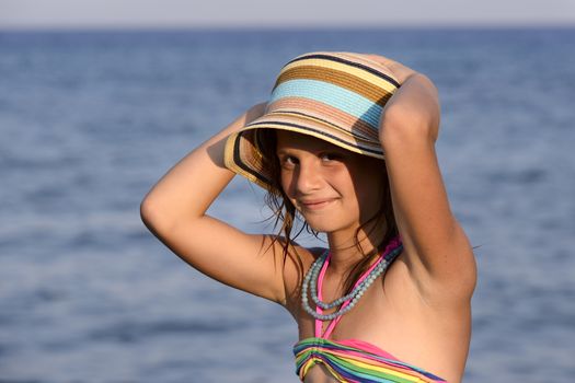 Little girl on the beach at sunset, portrait smiling with a large hat.