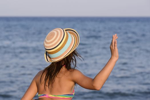 Little girl on the beach at sunset, gesticulating with her hand in greeting.