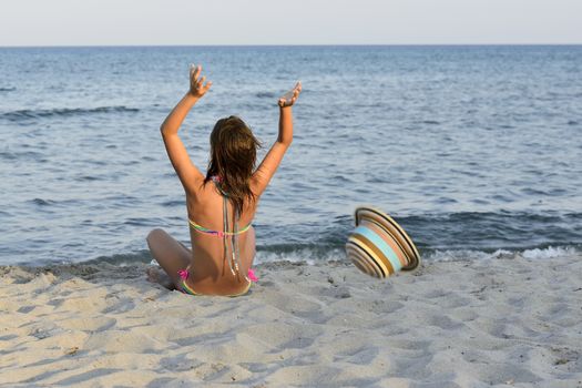Little girl on the beach at sunset, with har hands blocking a large hat.