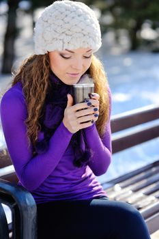 Young beautiful girl sitting on the bench in winter forest