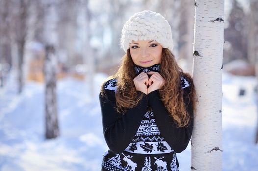 beautiful girl in white hat stands near the birch in winter