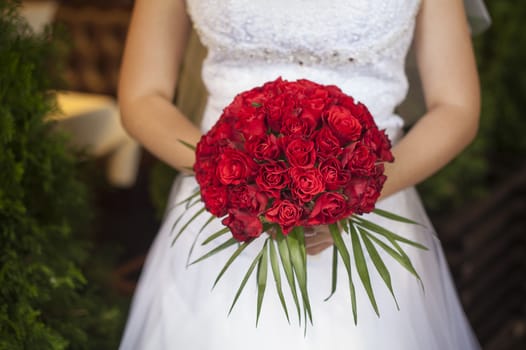 wedding bouquet of red roses and leaves in brides hands