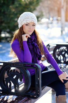 Girl in white hat sitting on a bench in winter