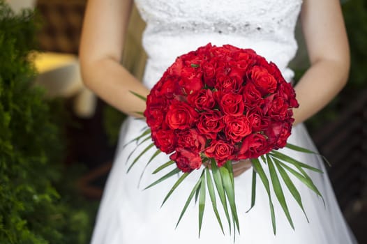 wedding bouquet of red roses and leaves in hand of bride