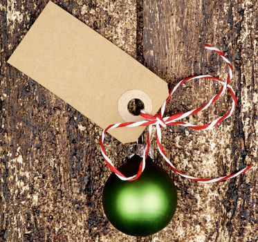 Christmas Decoration with Green Bauble, Striped Bow and Gift Card Note closeup on Textured Wooden background