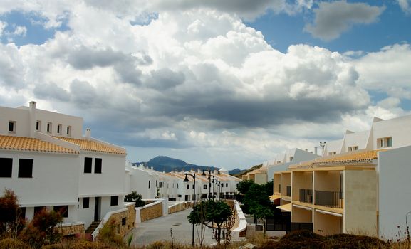 Classic Small Menorca Urbanization with White Houses under Cloudy Skies Outdoors. Balearic Islands