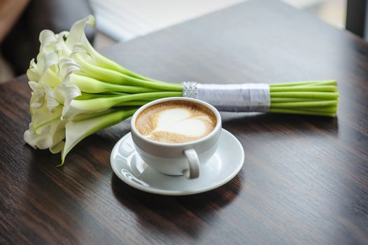 Wedding bouquet of calla lilies on a table with a cup of coffee