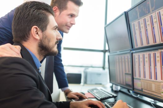 Businessmen trading stocks. Stock traders looking at graphs, indexes and numbers on multiple computer screens. Colleagues in discussion in traders office. Business success concept.