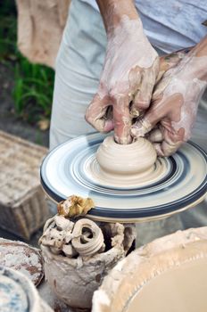 The hands of a potter help the child make a pitcher on a pottery wheel