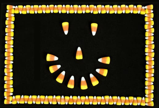 Happy face made from candy corn on black background and candy corn as a border.