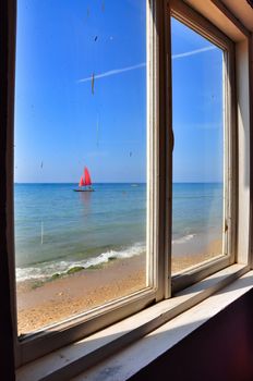 View from the window of an old thrown house on a boat with red sails, located on the Black Sea coast