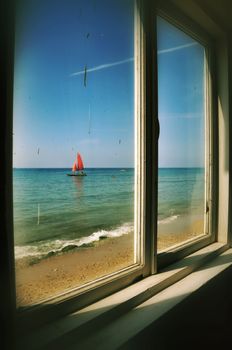 View from the window of an old thrown house on a boat with red sails, located on the Black Sea coast