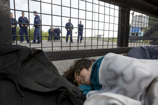 SERBIA, Horgos: A refugee child sleeps behind a border fence as Hungarian border guards appear in the background at the Serbia-Hungary border after Hungary closed the border crossing on September 16, 2015.****Restriction: Photo is not to be sold in Russia or Asia****