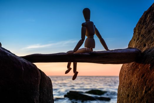 Wooden mannequin sitting on a stick between boulders