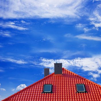 Red roof of new detached house against blue sky.