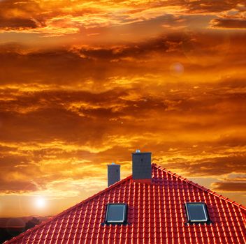 Red roof of new detached house against red sky.