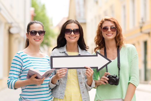 tourism, travel, vacation, direction and friendship concept - smiling teenage girls with white arrow showing direction outdoors