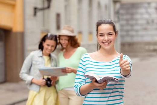 tourism, travel, holidays and friendship concept - smiling teenage girls with city guide, map and camera showing thumbs up outdoors