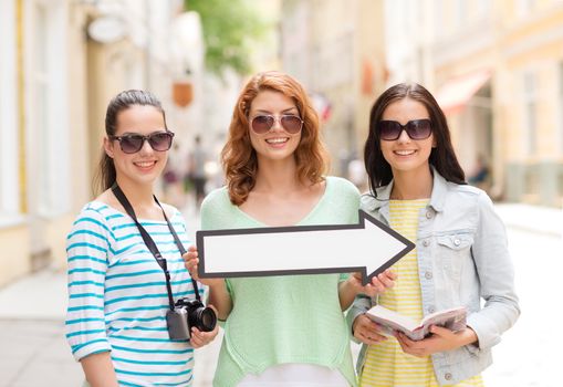 tourism, travel, vacation, direction and friendship concept - smiling teenage girls with white arrow showing direction outdoors