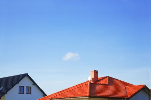 Red roof of new detached houses against blue sky.