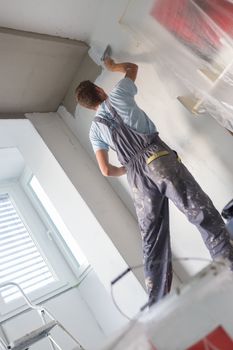 Thirty years old manual worker with wall plastering tools inside a house. Plasterer renovating indoor walls and ceilings with float and plaster.