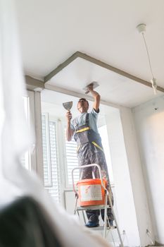 Thirty years old manual worker with wall plastering tools inside a house. Plasterer renovating indoor walls and ceilings with float and plaster.