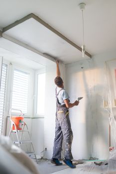 Thirty years old manual worker with wall plastering tools inside a house. Plasterer renovating indoor walls and ceilings with float and plaster.