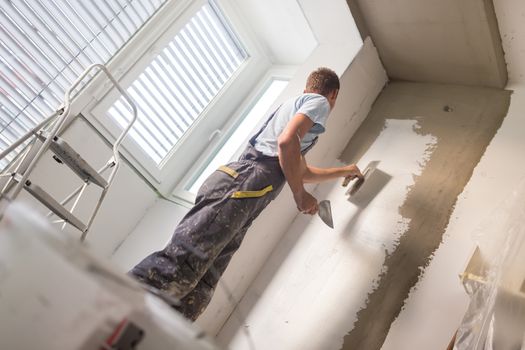 Thirty years old manual worker with wall plastering tools inside a house. Plasterer renovating indoor walls and ceilings with float and plaster.