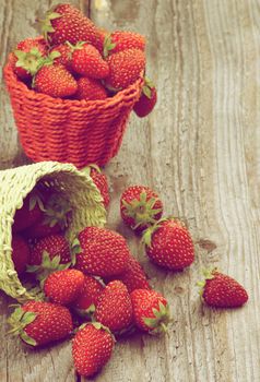 Ripe Forest Strawberries in Green and Red Wicker Baskets closeup on Rustic Wooden background. Retro Styled