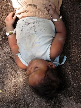 A poor little child sleeping under the sun and shade in the soil used for construction.                               