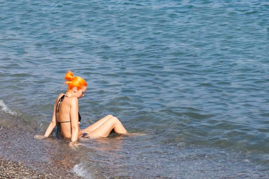 ALUSHTA,RUSSIA-September 06:beautiful the girl sits on the seashore,RUSSIA-SEPTEMBER 06 2015.In the Crimea many people sunbathe on the bank of the Black Sea