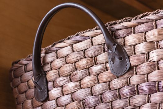 A close up shot of a brown wicker basket with a leather handle stitched onto it