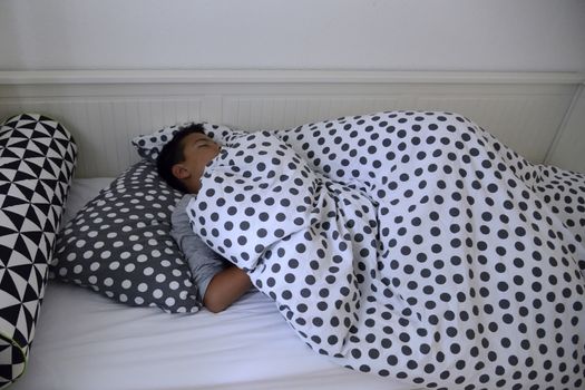 Diffused natural light dark. The child asleep in the night in his bed with sheets with polka dots.