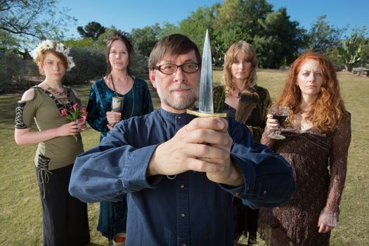 Serious male pagan priest with group and dagger outdoors