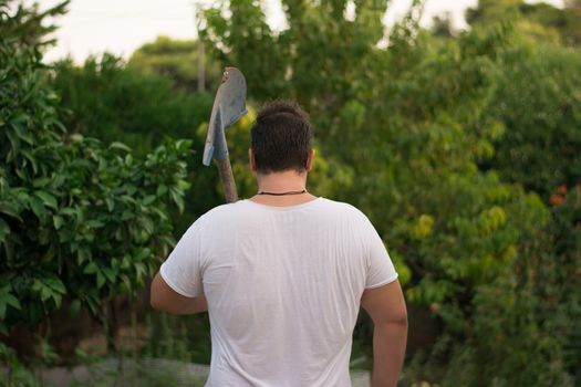 Young farmer walking away with a shovel on his back.