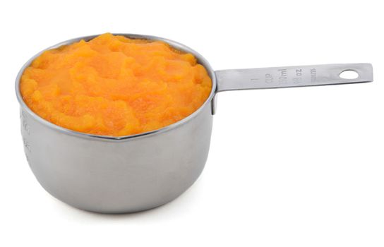Pureed pumpkin in an American measuring cup, isolated on a white background