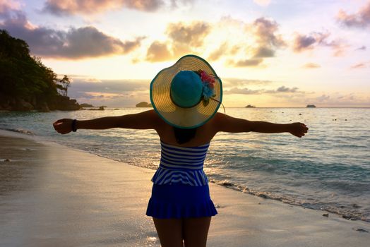 Tourist girl in a swimsuit blue and white striped hat standing on beach with pleasure the beautiful landscape of sky and sea during sunrise, Miang island, Similan National Park, Phang Nga, Thailand
